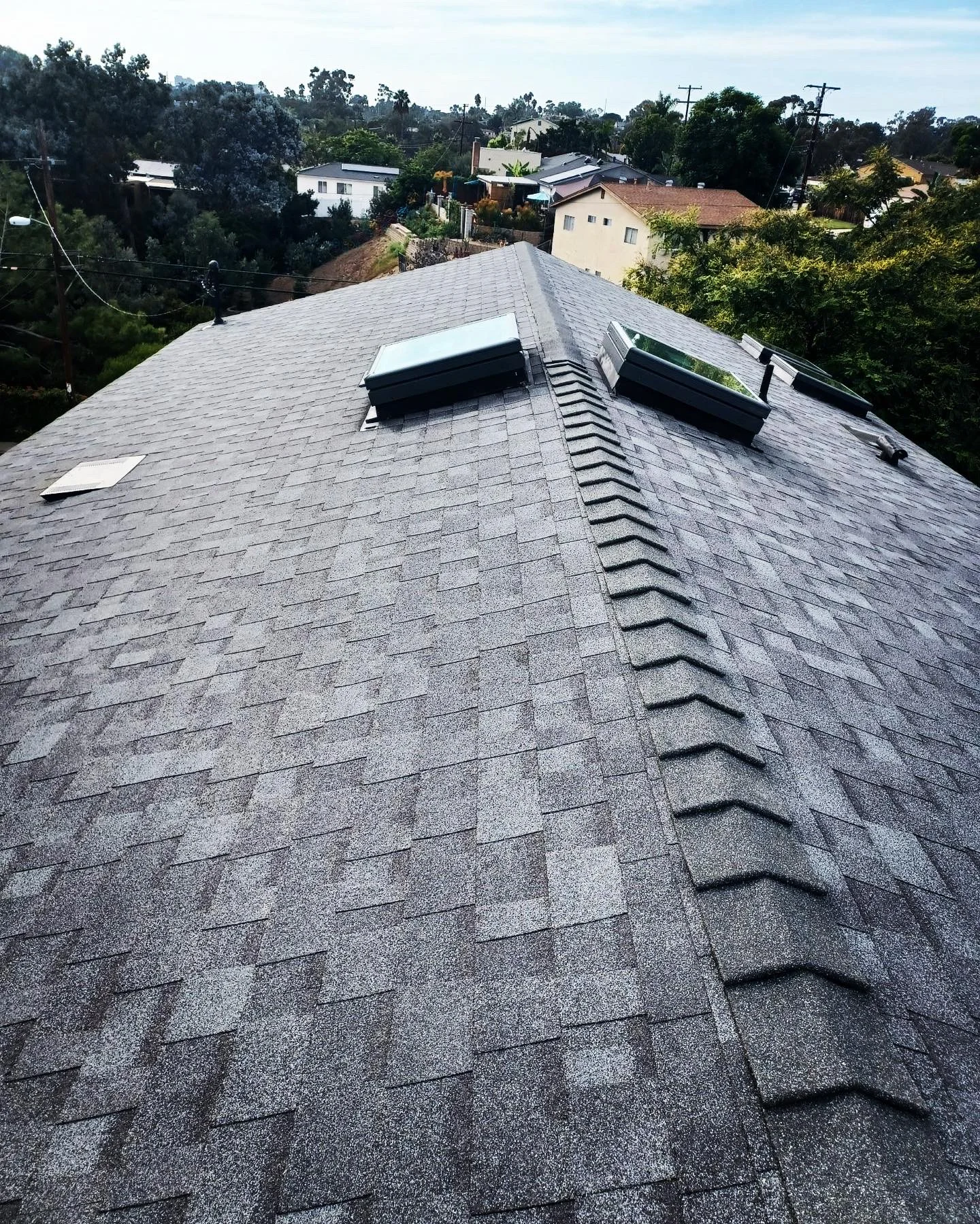 Newly installed gray architectural asphalt shingle roof with ridge vents and roof penetrations