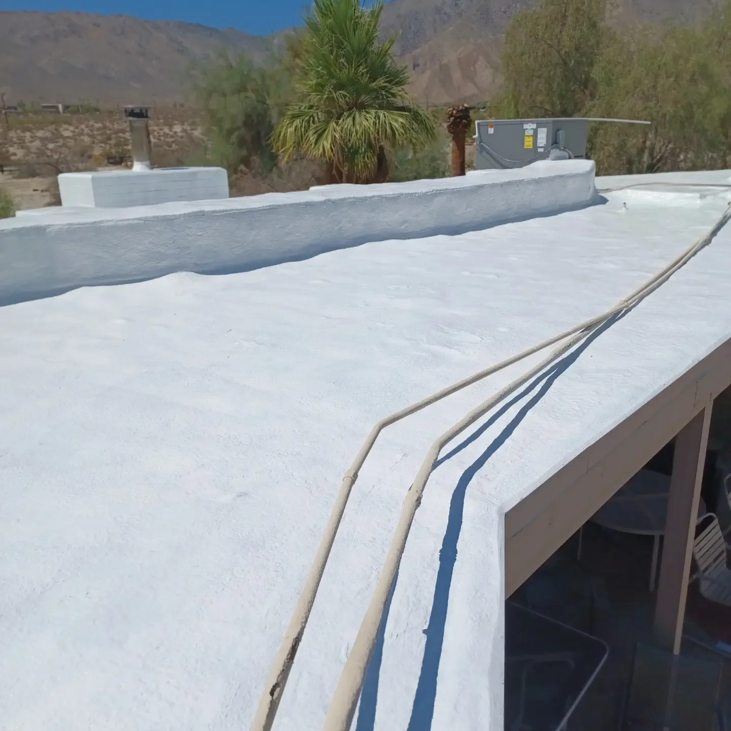 White flat roof with curved parapet walls and blue drainage lines in desert setting
