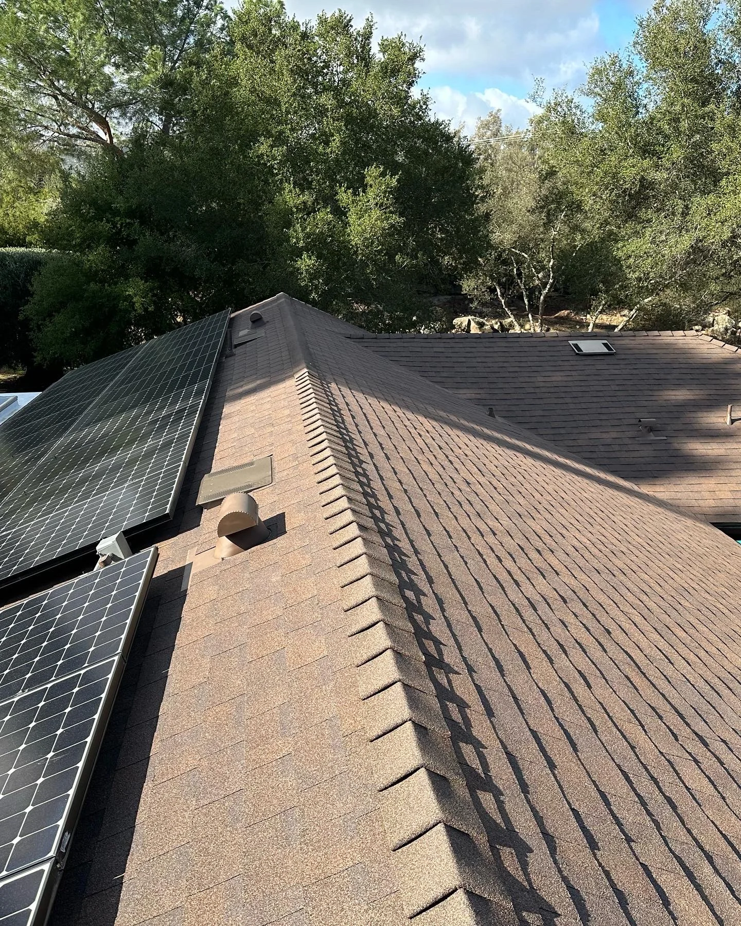 Newly installed brown asphalt shingle roof with solar panels and proper ventilation