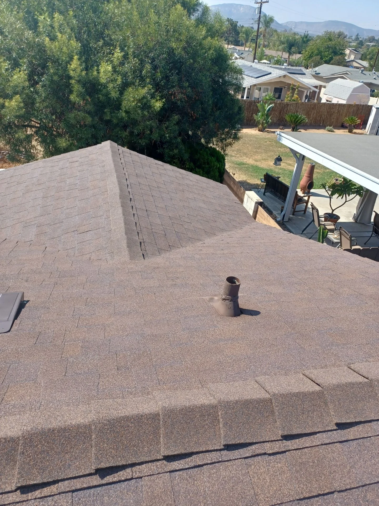 Newly installed gray asphalt shingle roof with ridge caps and vent pipe flashing on residential home