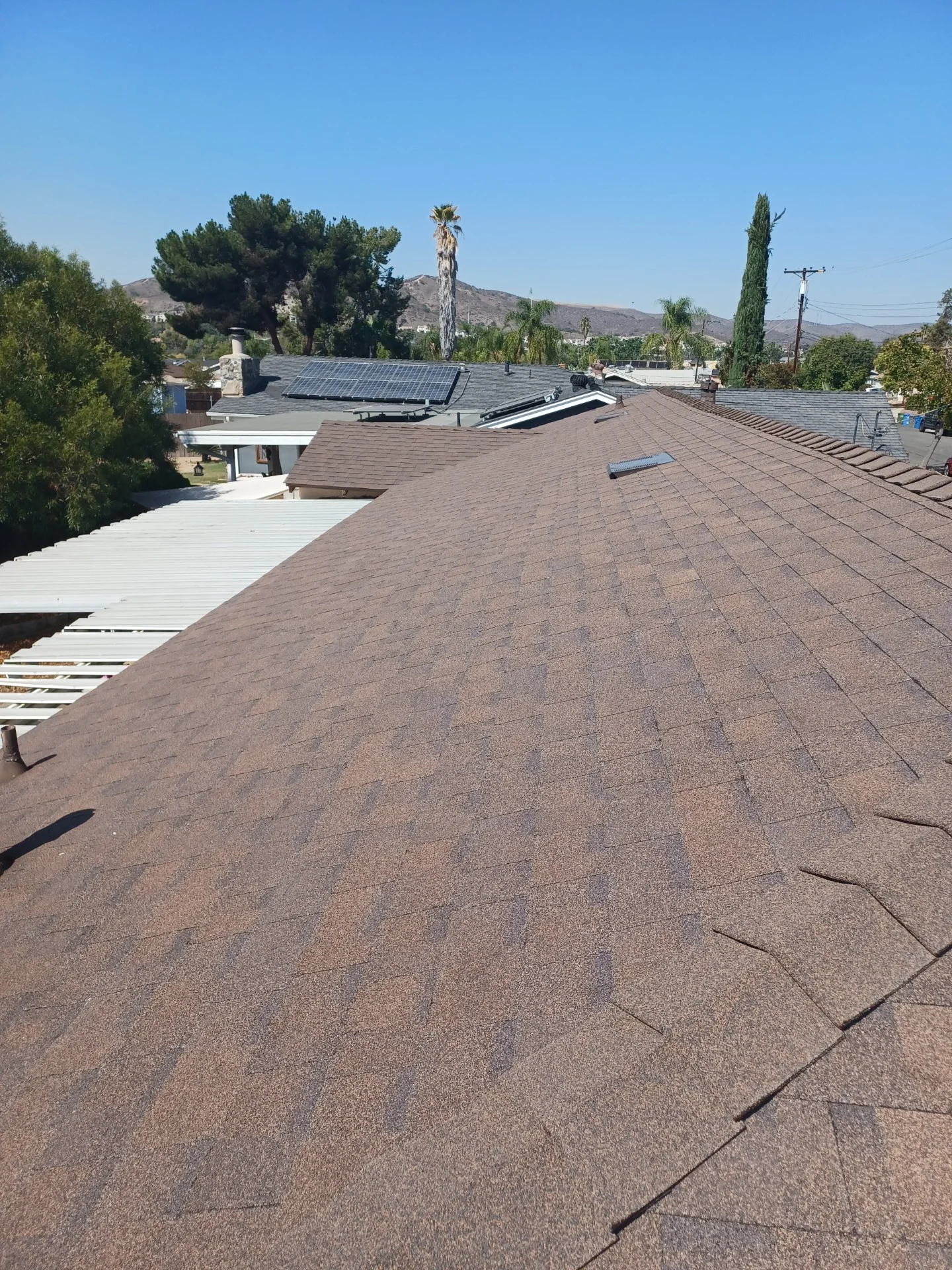 Newly installed brown asphalt shingle roof on residential home with solar panels and mountain views