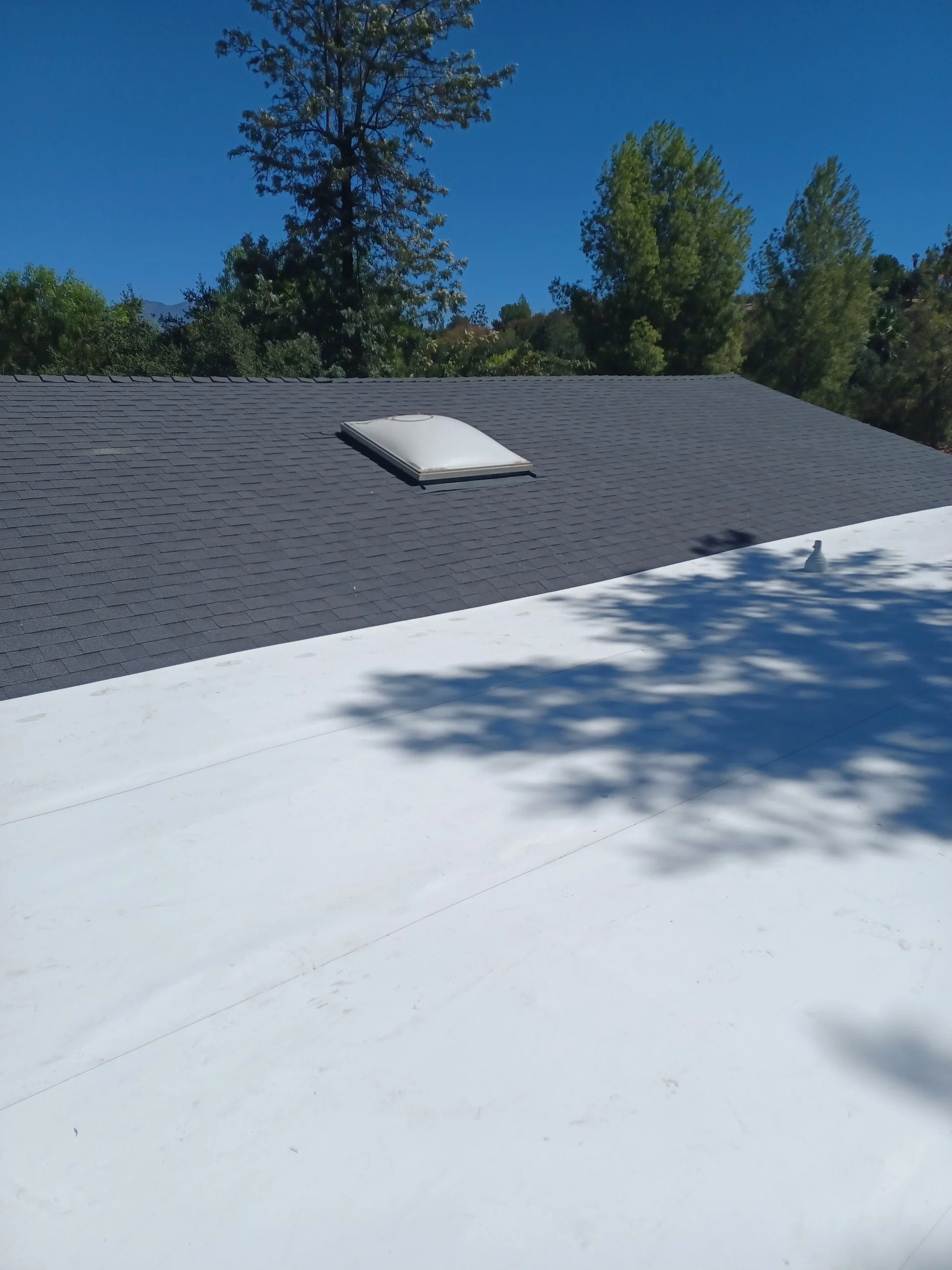 New gray asphalt shingle roof with white skylight dome on residential home