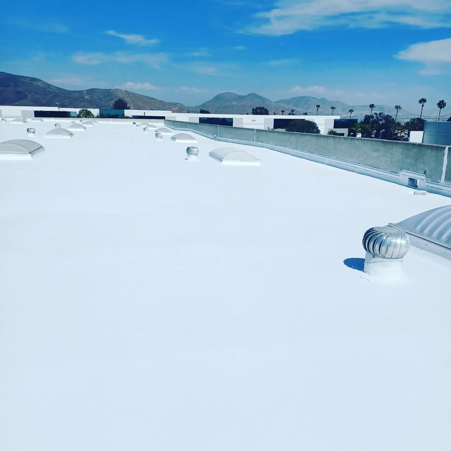 White flat roof with ventilation turbines and concrete parapet overlooking San Diego mountains
