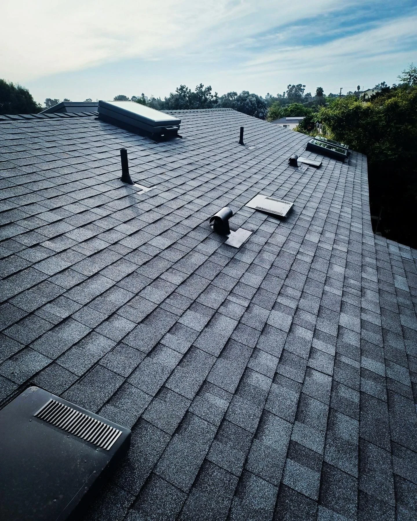 Newly installed charcoal gray asphalt shingle roof with vents and skylights