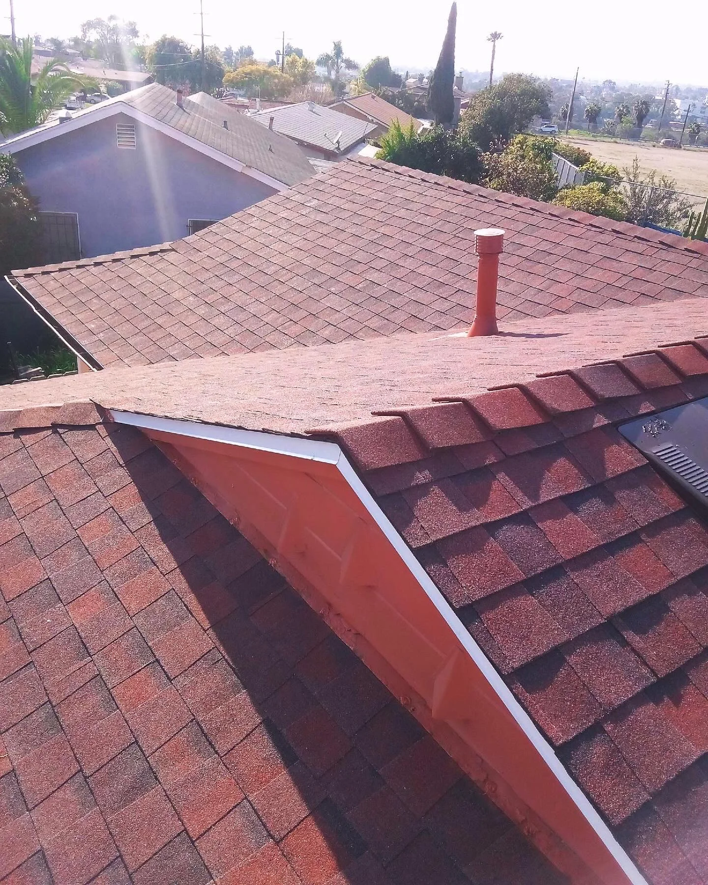 Newly installed burgundy architectural shingle roof with red flashing and white trim on residential home