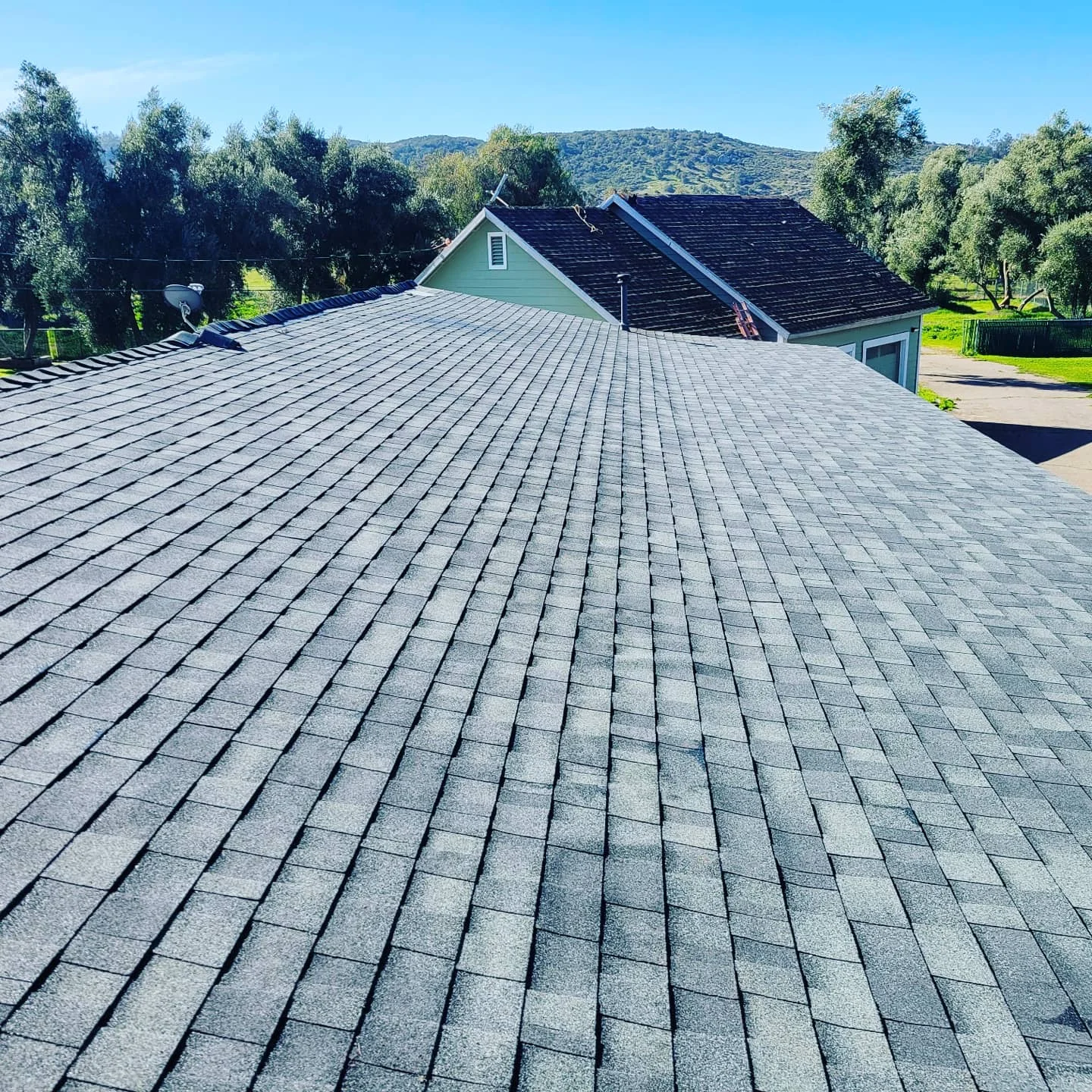 New gray asphalt shingle roof on residential home with gable design and hillside backdrop