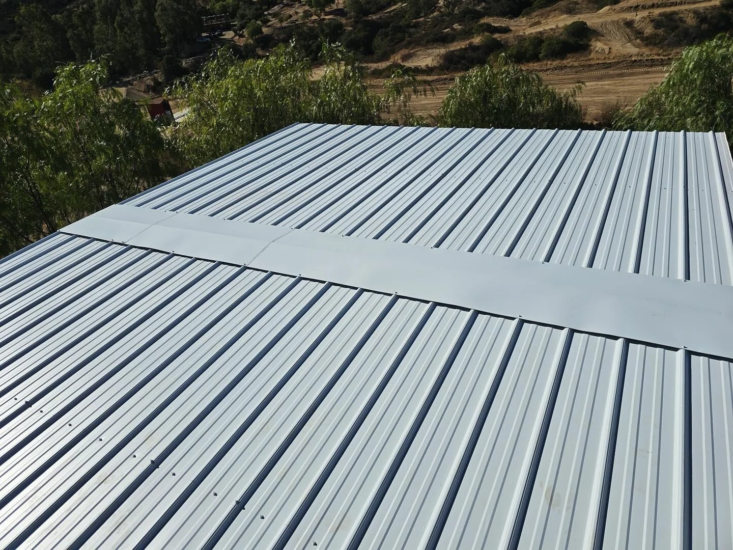 Light gray standing seam metal roof with parallel corrugated panels and ridge cap detail
