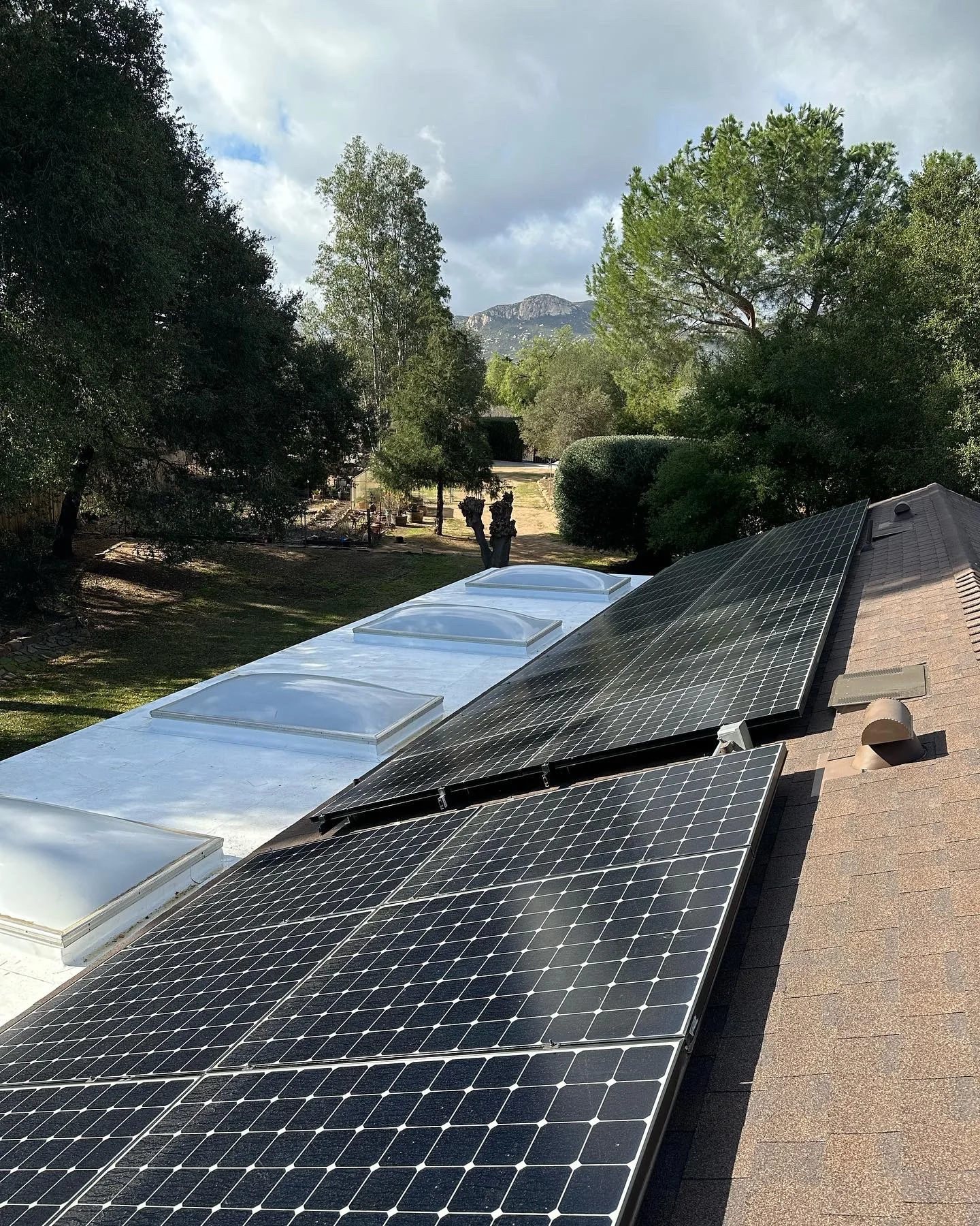 Solar panels and skylights installed on pitched residential roof with mountain backdrop