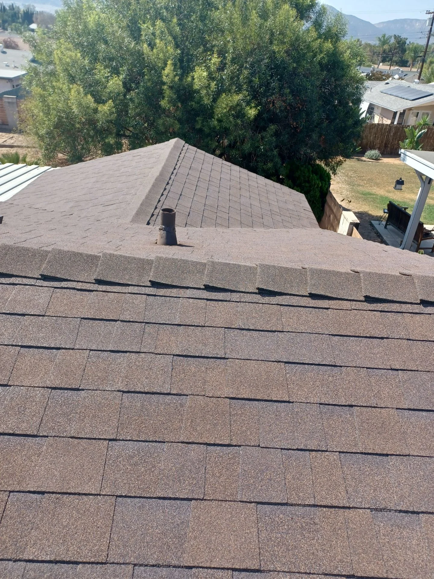 Newly installed gray asphalt shingle roof with ridge cap and vent on residential home