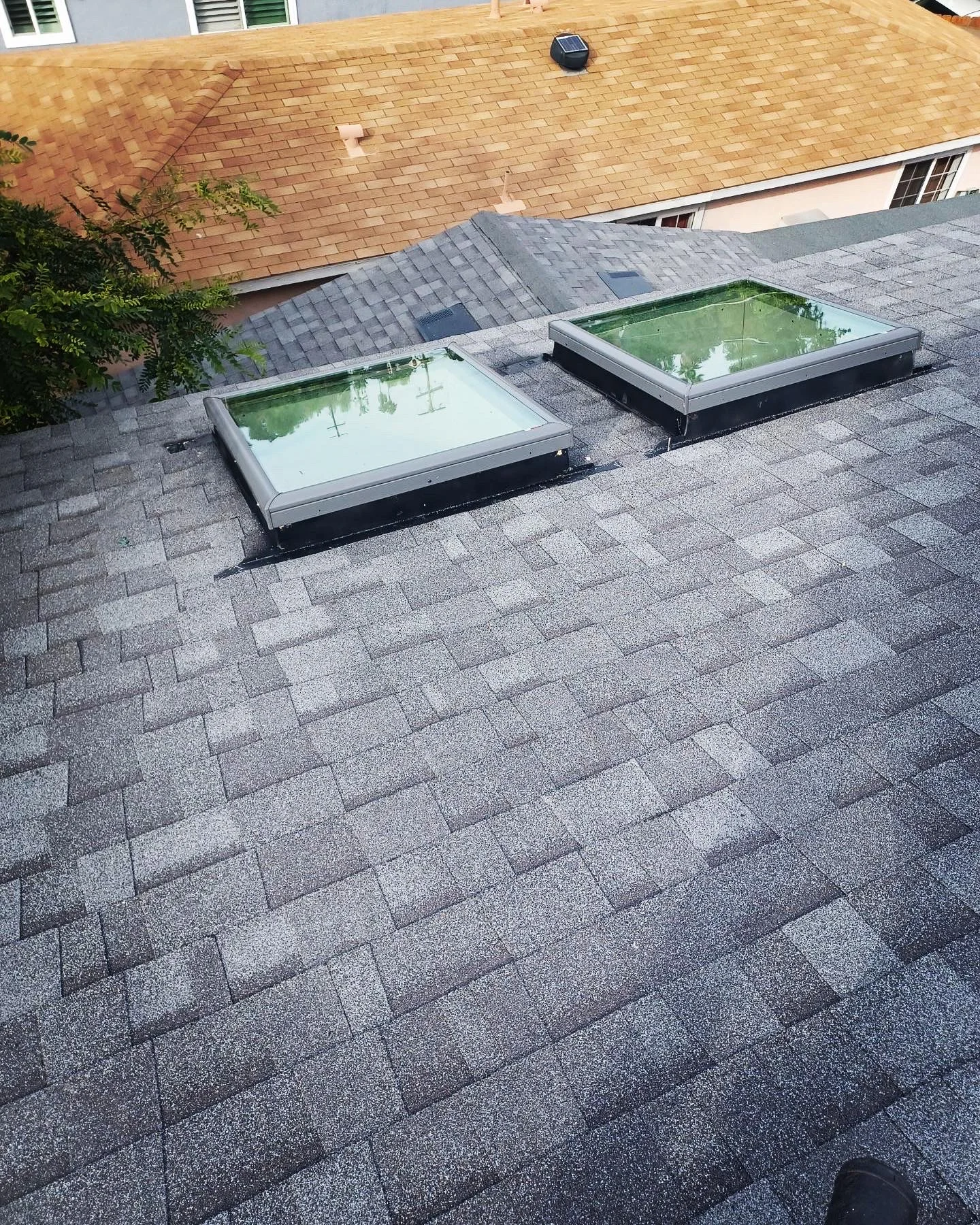 Newly installed flat roof with two skylights and gray asphalt shingles on residential home