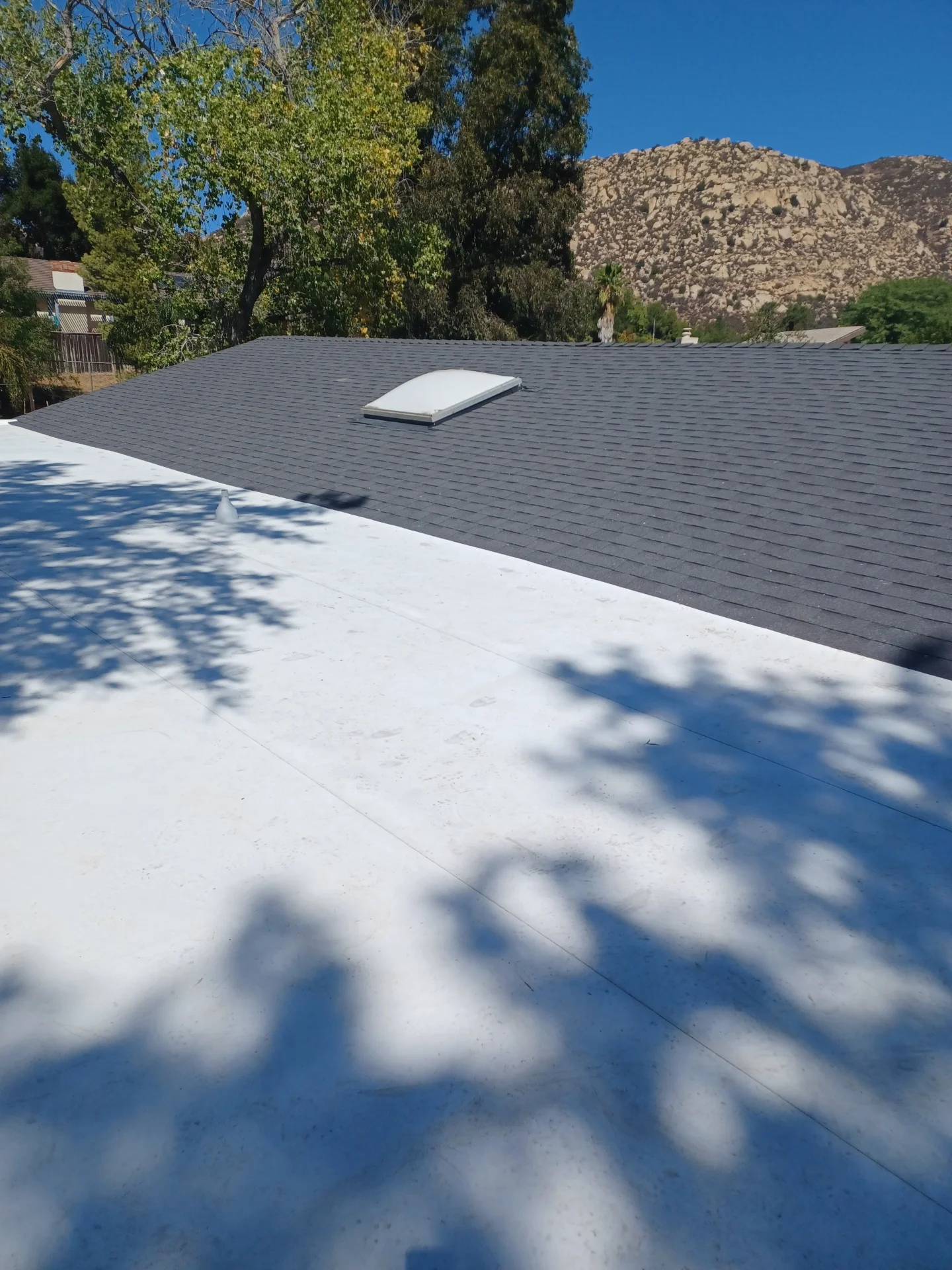 New gray asphalt shingle roof with white skylight installed, mountain backdrop visible