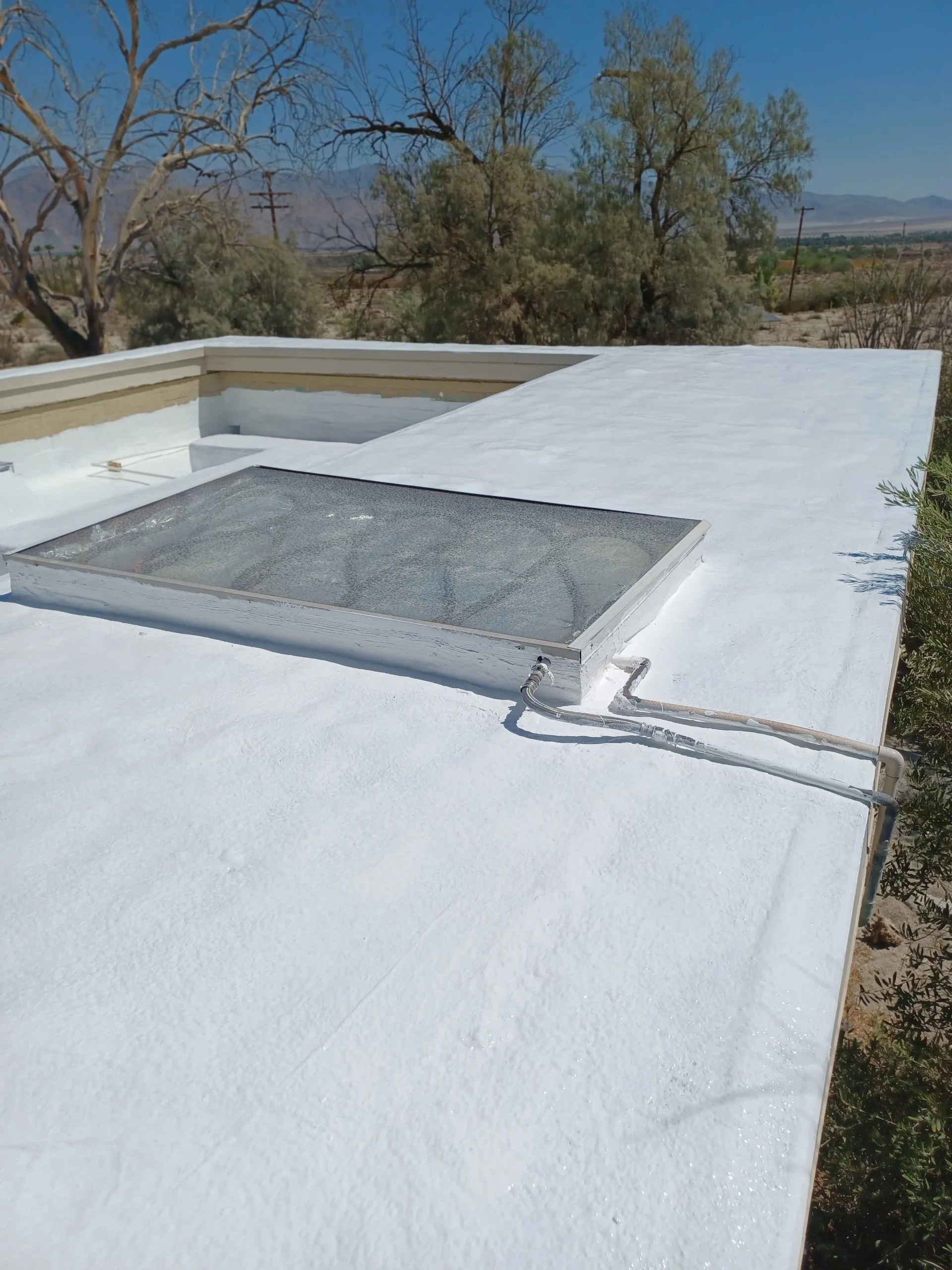 White flat roof membrane with skylight opening and metal flashing on desert hillside